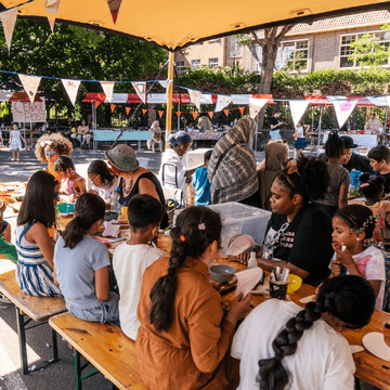 Mensen zitten aan een tafel tijdens het Bloemhof Festival 2025 op het Putselaan-complex